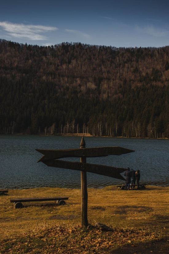 A wooden sign in front of a lake points in different directions.