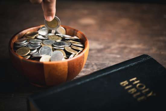 An Adventist places his offering in a offering bowl beside the Bible.