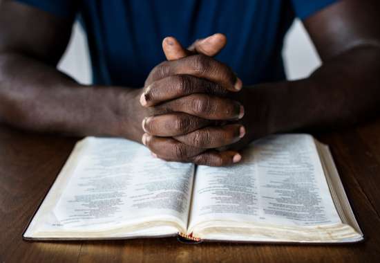 An image of hands folded in prayer over an open Bible.