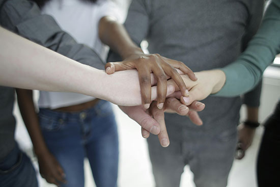 A group of men stand in a circle and stack their hands in the center to demonstrate unity and teamwork.