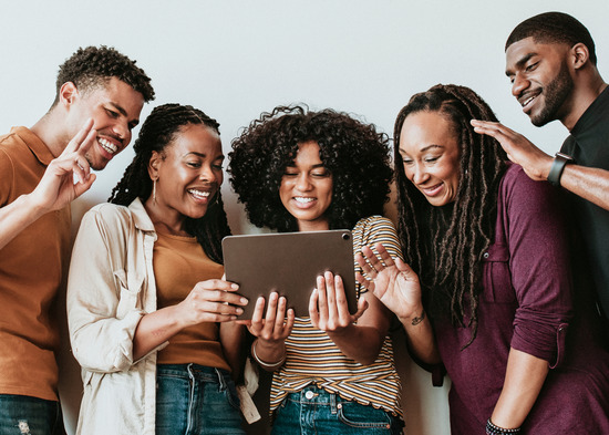 A group of young people gather around a digital tablet to wave at a friend they've video called.