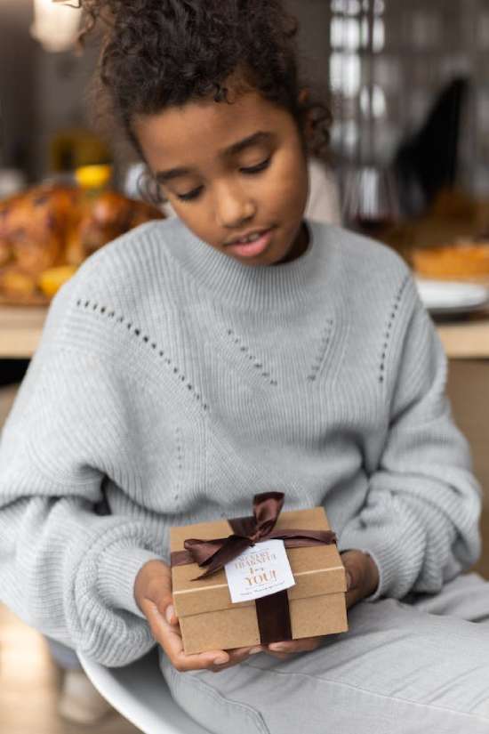 A young girl looks down at a gift box that she holds in her hands. This illustrates that sometimes, God's answers to our prayers and His gifts to us are sometimes things we don't expect or understand yet.