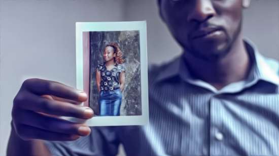 A man with a sad look on his face holds up a photo of a woman, perhaps a loved one that he lost recently.