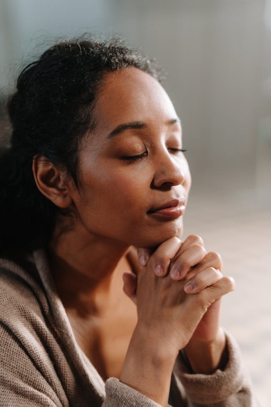 A woman with closed eyes clasps her hands and tilts her head upward in prayer.