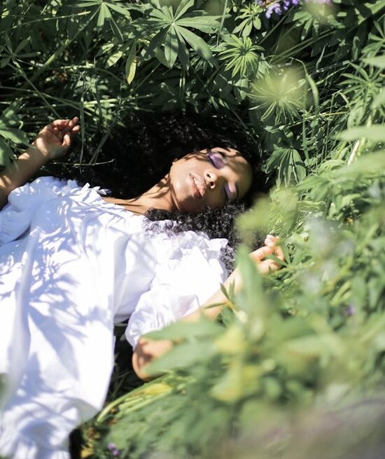A woman in a white dress lies in a bed of grass, enjoying the beauty of nature. 