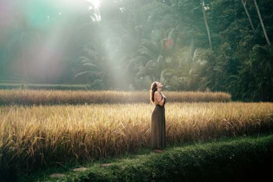 A woman standing in a field of grain and breathing deeply as she looks up to the sky