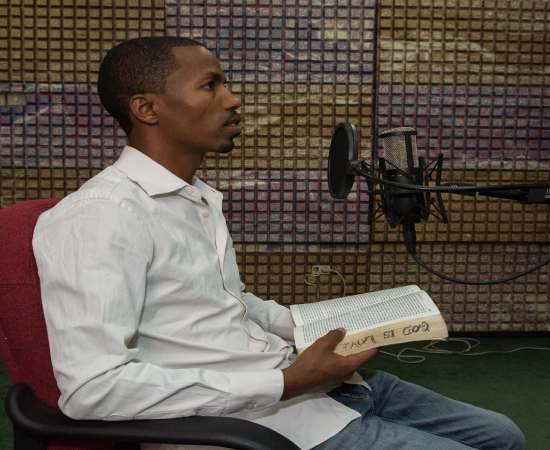 An Adventist media anchor speaking into a microphone and broadcasting the gospel