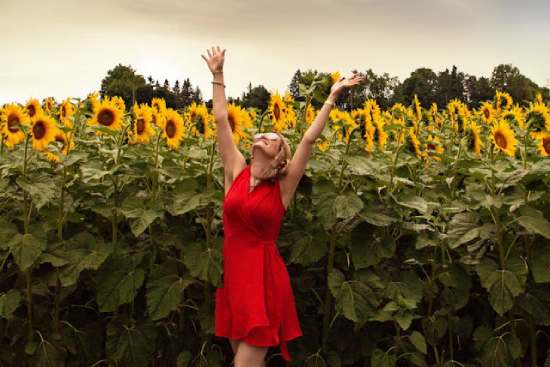 A woman in a field of sunflowers with her hands outstretched toward the sky