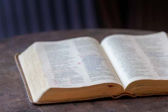 An image of the Bible, resting on a table, opened to a specific passage.