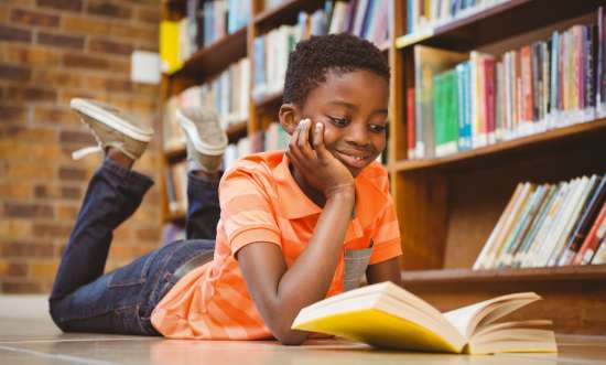 A young boy reads a book with a smile on his face, showing how important it is to have positive reading material, no matter your age.