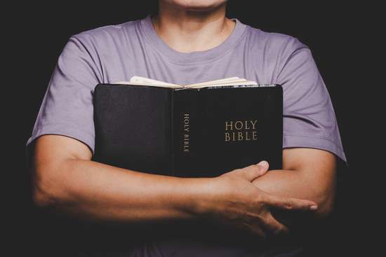 A person holds an open Bible close to their chest as they pray.