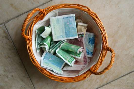 An overhead photo of a basket filled with money. These bills may have just been collected in a church service, illustrating how tithe and offering help to support the church from the bottom up.