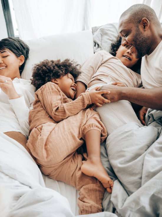 A family laughing and resting together in bed, relaxing Sabbath morning