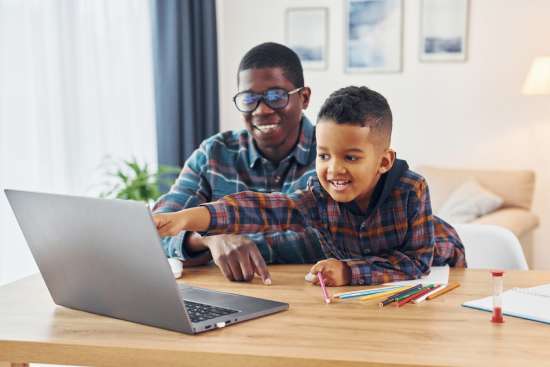 A father is using a laptop computer to research schools and his son is pointing at something on the screen