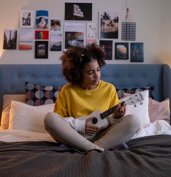 A young woman sits in a bed with a guitar. She may be singing praises to God, something Adventists do at Vespers.