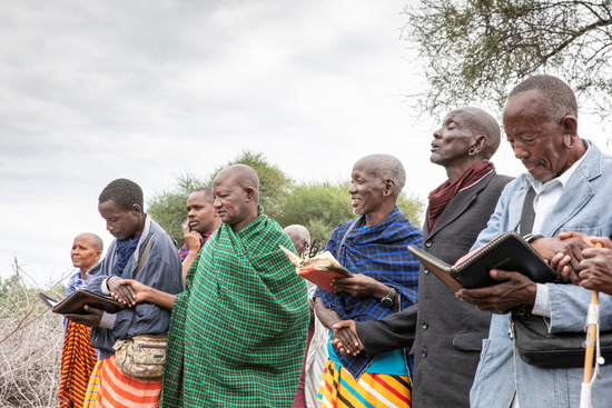  A group of people worship together outside with their Bibles open. Studying together is one feature of Adventist adult programs.