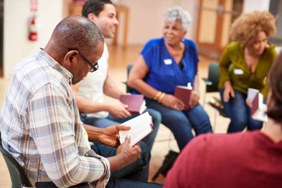 A group of people sit in a circle and engage in group Bible study. Groups studies can help strengthen our relationship with God and others.