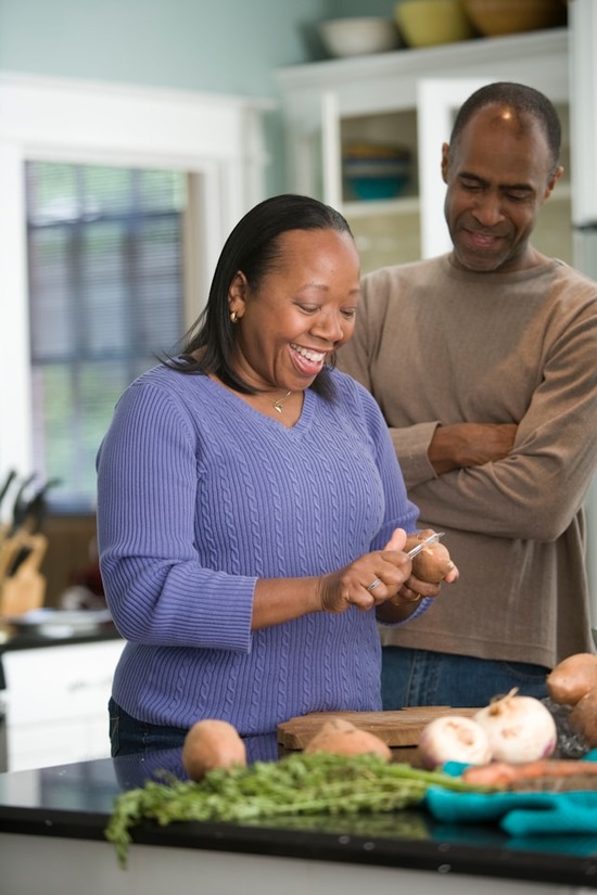 An older couple smiling and peeling potatoes in the kitchen