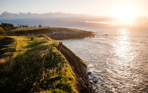 Green fields near seashore and sun setting at the horizon as we discuss how God established Sabbath during the Creation week.