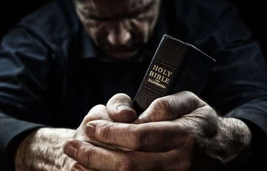 A man holding a Bible and praying to Jesus