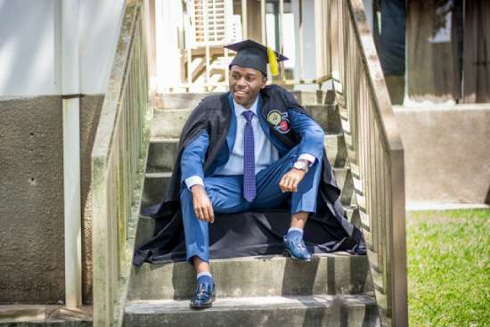  A young man in graduation cap and gown sitting on some steps and celebrating the completion of his master's in divinity