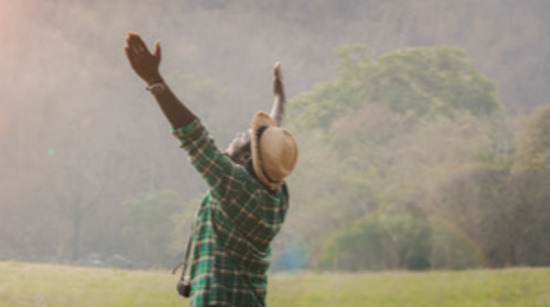 A man in a field lifts his hands in prayer, exhibiting one of the many positions you can pray in.