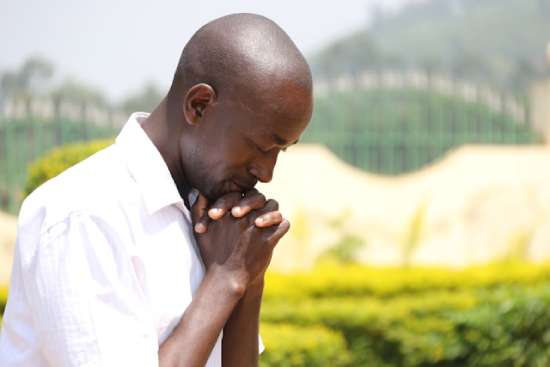 A man prays with folded hands in a field of flowers. Being in nature and praying are healing for the soul.