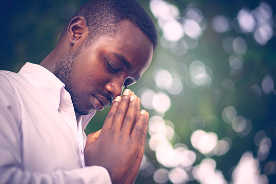 A man bows his head and folds his hands in prayer.