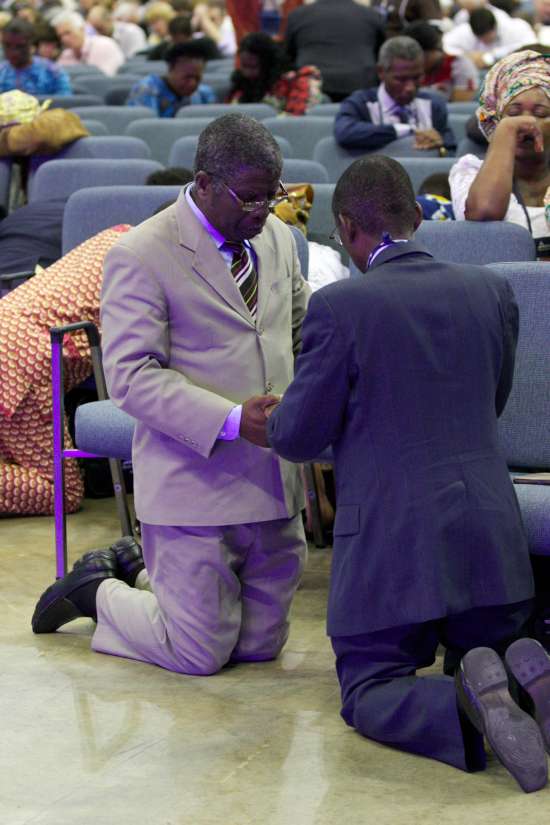 Two men in church kneeling in prayer. They are facing each other and holding hands, showing how we can pray together when we need God to give us discernment.