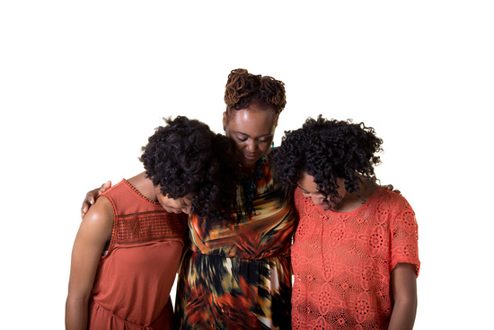 Three women bow their heads and put their arms around each other in prayer. Praying together can strengthen our relationships with God and others.