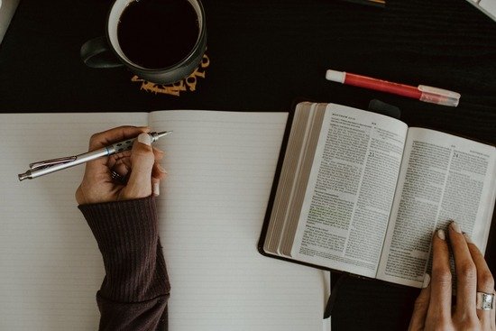 Two hands, one on an open Bible and the other about to write in a notebook. When we turn to God's Word for guidance instead of trying to reason with the devil, we can experience freedom from temptation.