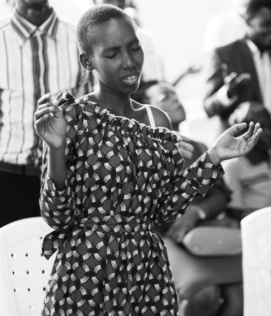 A young woman attending a church service lifts her hands in praise and in prayer. She may be praying the lyrics of a song to God.