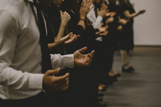 A group of people stand beside each other and hold their hands open to represent their willingness to receive spiritual gifts.