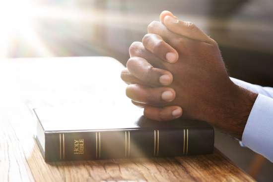 Hands clasped in prayer over a Bible, illustrating that prayer is an important part of individual and group Bible study.
