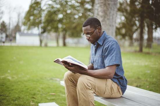 A young man sits on a set of bleachers outside and reads the Bible, illustrating how Bible prophecy can give us a unique perspective on life.