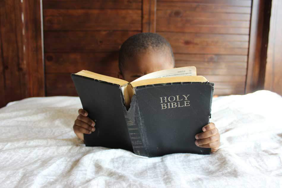A young child reading the Holy Bible intensively and with much interest 