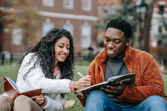 Two Adventist college students sit next to each other, helping each other study Show less