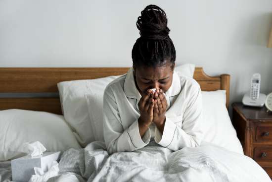 A woman cloaked in a blanket blows her stuffy nose, showing that a lack of rest often leads to sickness.
