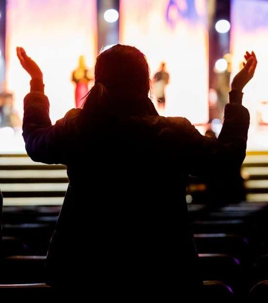 A woman in a church service raises her hand in praise to God.