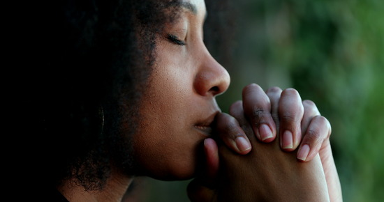A woman with her hands clasped in sincere prayer.