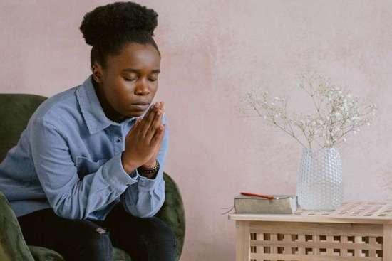 A woman clasps her hands and bows her head in prayer.