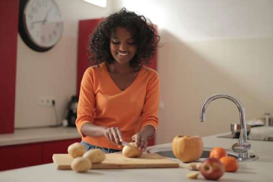 A young woman smiles while chopping vegetables. Her colorful diet exemplifies Ellen White's counsel on healthy living.