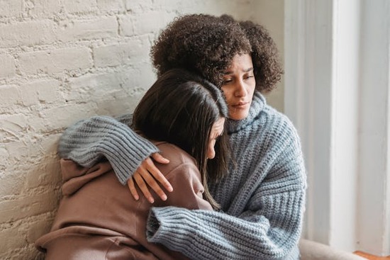 Two women grieve together, holding each other in comfort