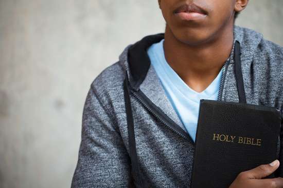 A close up of a young man’s upper body, holding a Bible close to his chest.