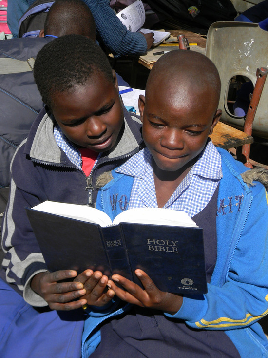 Two young kids read the Bible with a smile on their face
